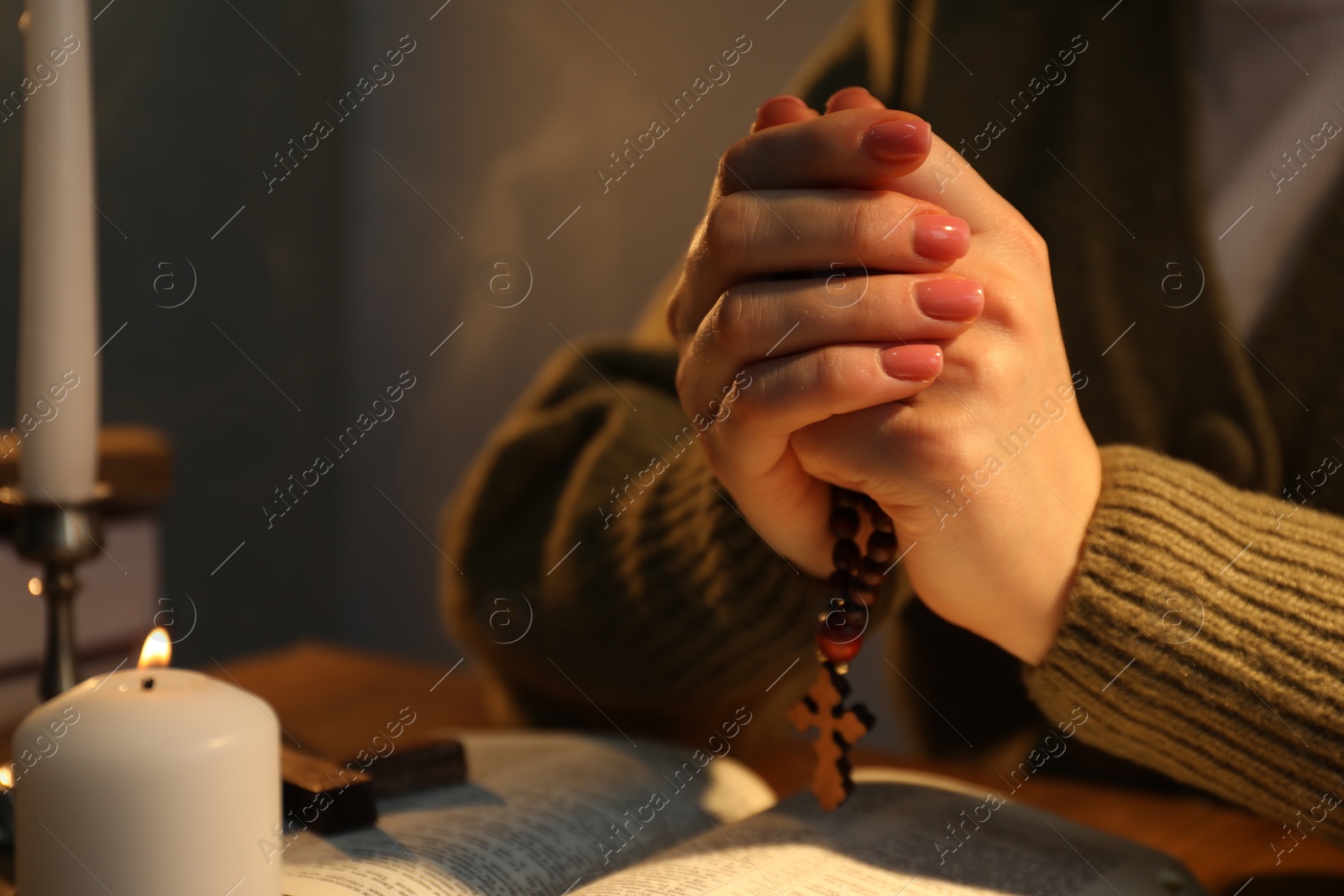 Photo of Woman praying at table with burning candle and Bible, closeup