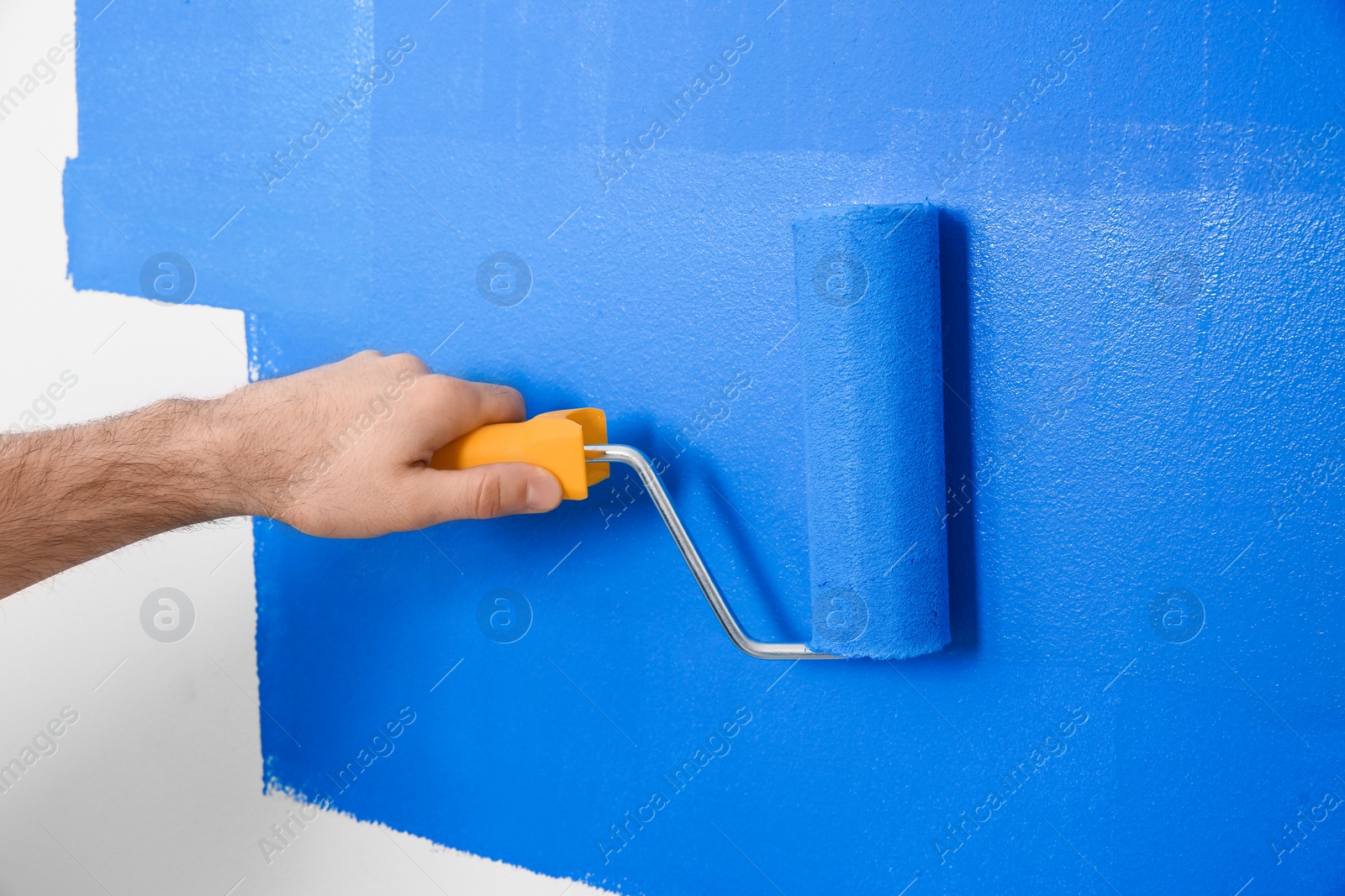 Photo of Man painting white wall with blue dye, closeup. Interior renovation