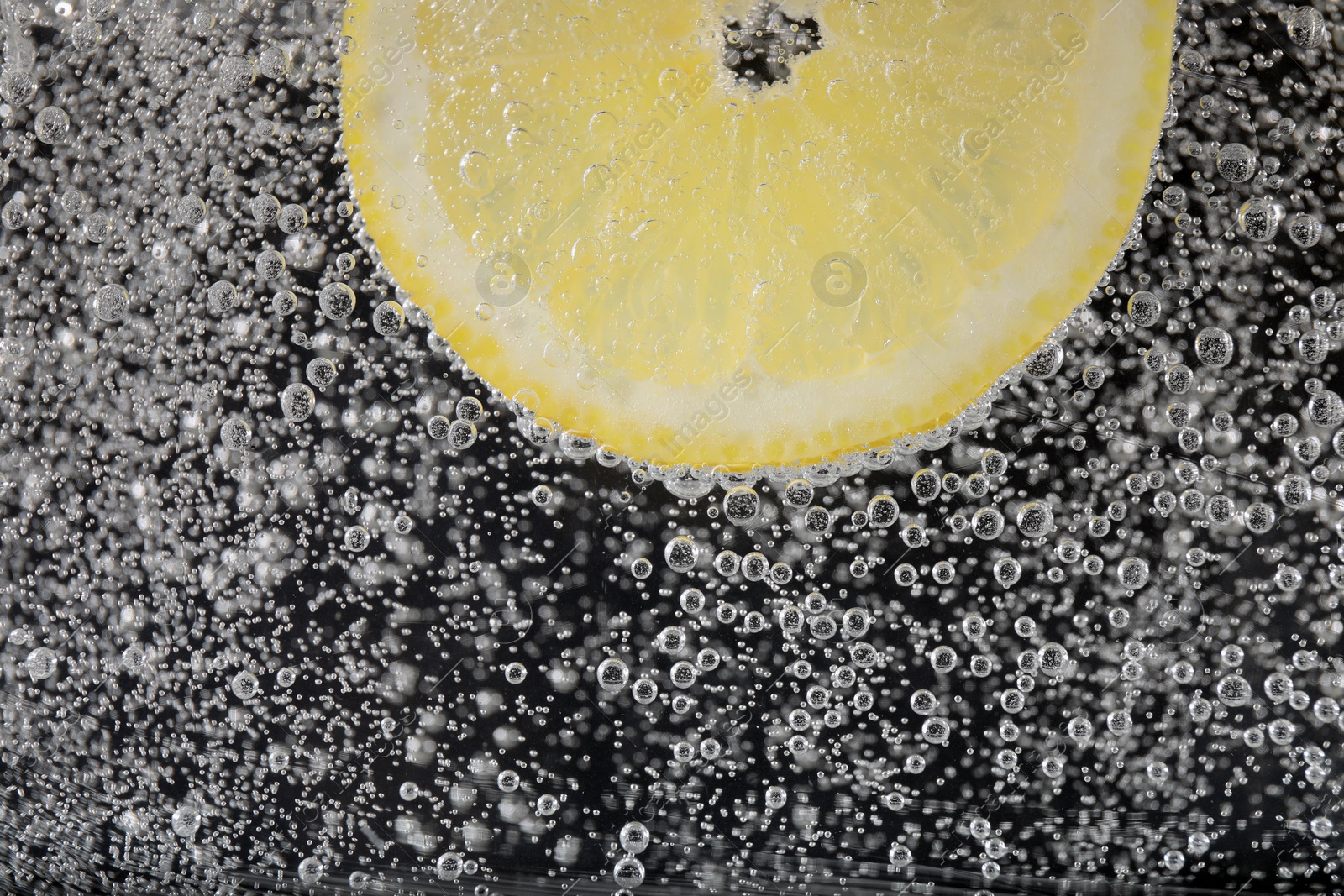 Photo of Juicy lemon slice in soda water against black background, closeup. Space for text