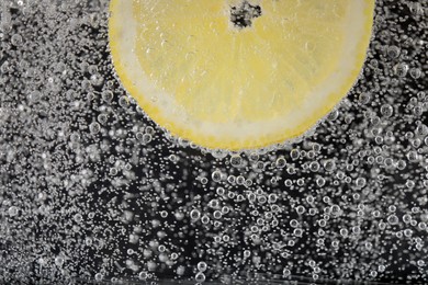 Juicy lemon slice in soda water against black background, closeup. Space for text