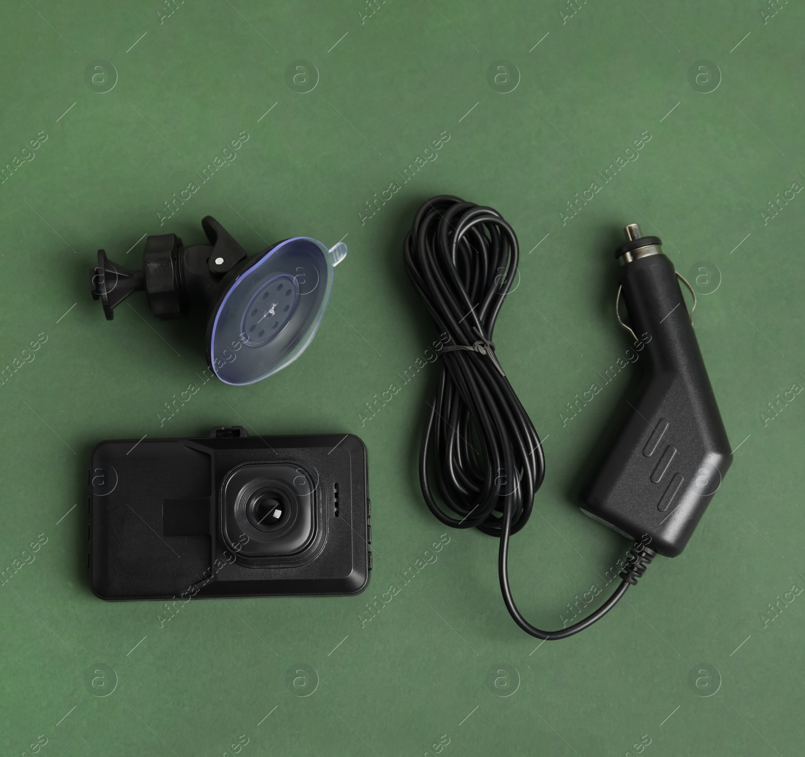 Photo of Modern car dashboard camera, suction mount and charger on dark green background, flat lay