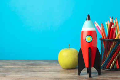 Photo of Bright toy rocket and school supplies on wooden desk. Space for text