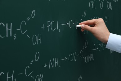 Photo of Teacher writing chemical formulas with chalk on green chalkboard, closeup