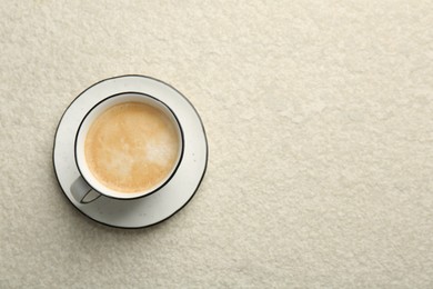 Photo of Tasty cappuccino in cup and saucer on light textured table, top view. Space for text