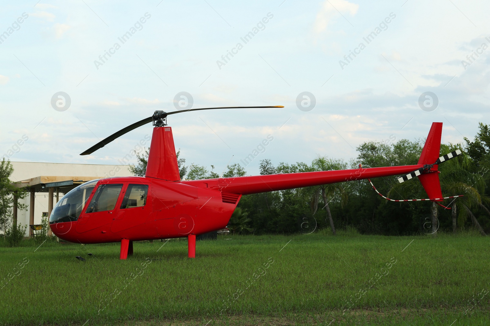 Photo of Modern red helicopter on green grass outdoors