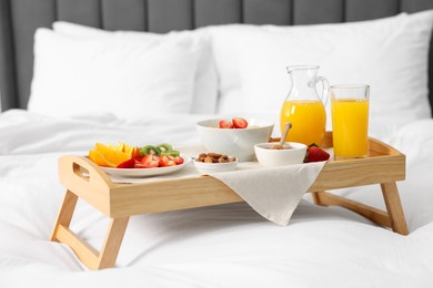 Photo of Wooden tray with tasty breakfast on bed at home
