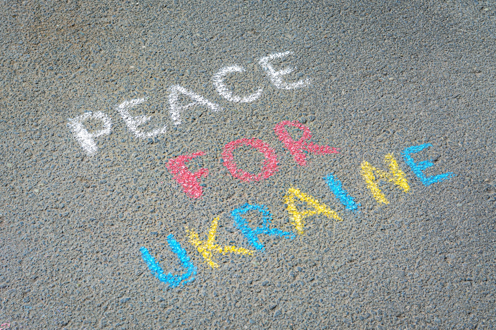 Photo of Words Peace For Ukraine written with colorful chalks on asphalt outdoors