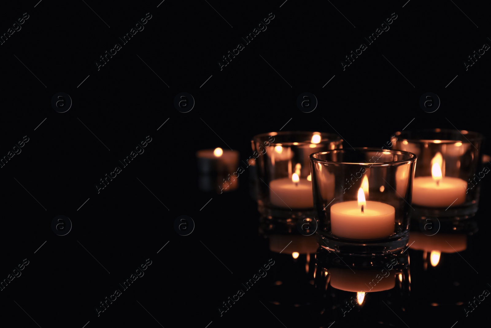 Photo of Burning candles in glass holders on dark background. Space for text