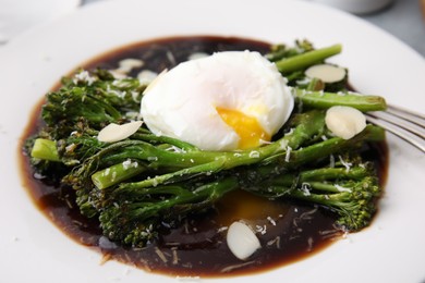 Photo of Tasty cooked broccolini with poached egg, almonds and sauce on plate, closeup