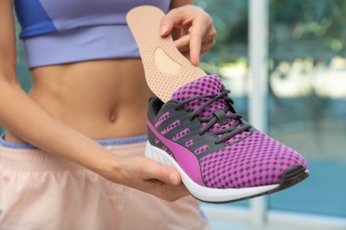 Woman putting orthopedic insole into shoe indoors, closeup. Foot care