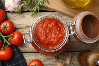 Photo of Homemade tomato sauce in jar and ingredients on wooden table, flat lay