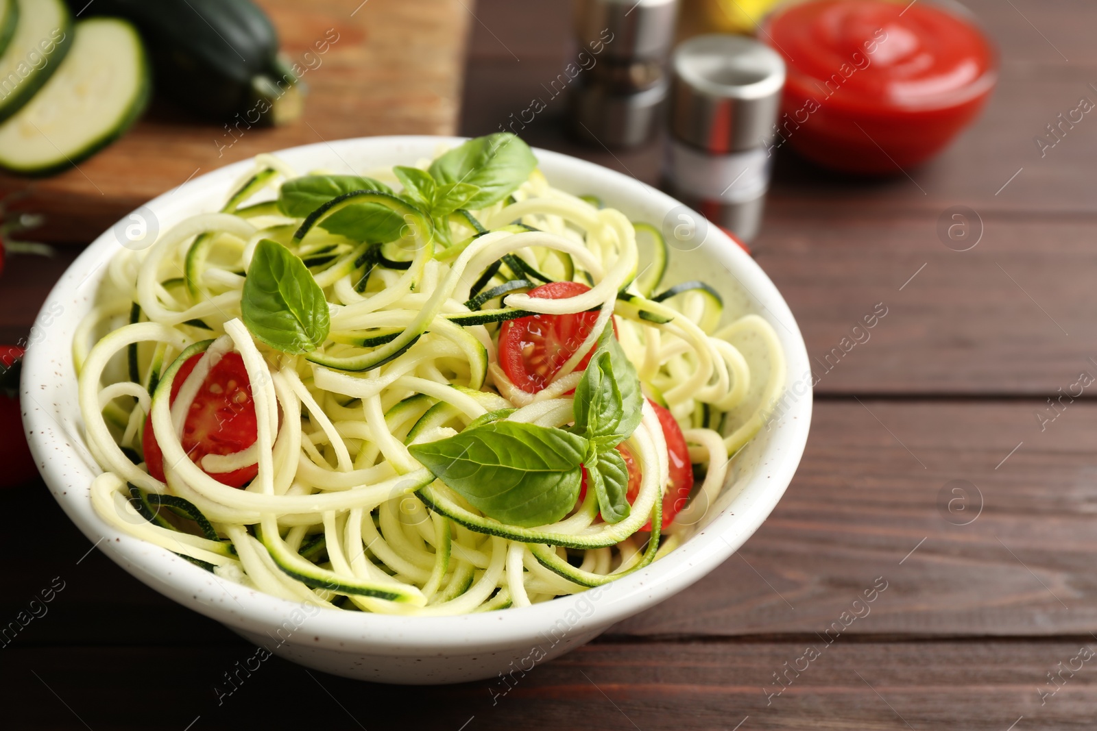 Photo of Delicious zucchini pasta with cherry tomatoes and basil in bowl on wooden table