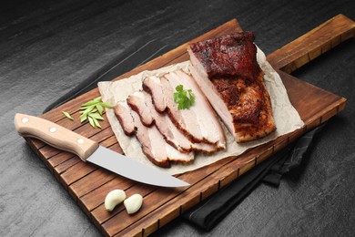 Photo of Pieces of baked pork belly served with parsley and garlic on black textured table