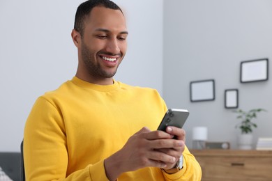 Photo of Happy man sending message via smartphone indoors