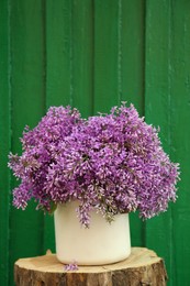Beautiful lilac flowers in vase on wooden stump against green background