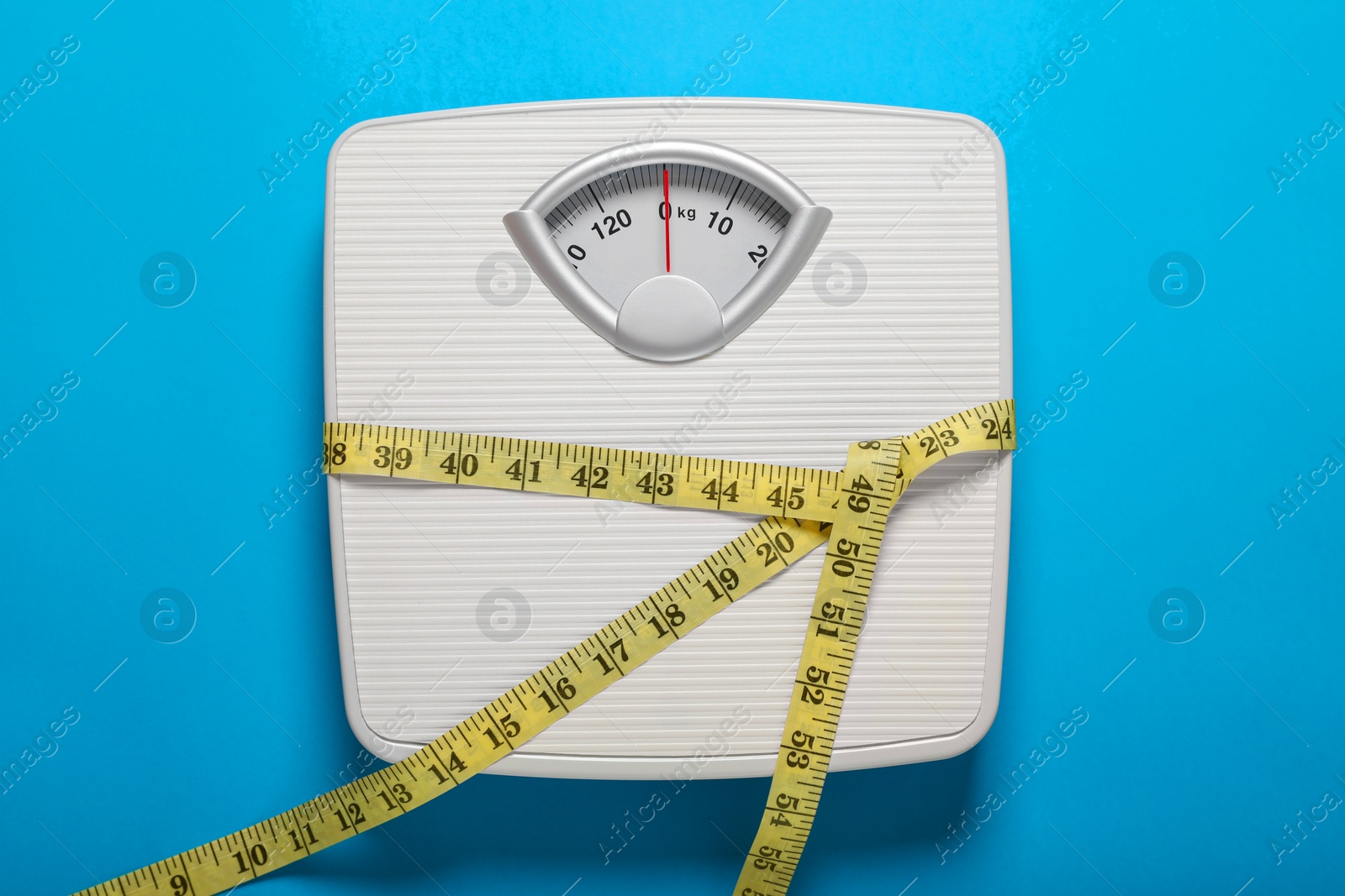 Photo of Bathroom scale tied with measure tape on light blue background, top view
