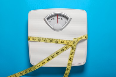 Bathroom scale tied with measure tape on light blue background, top view