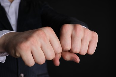 Photo of Businessman showing fists with space for tattoo on black background, closeup