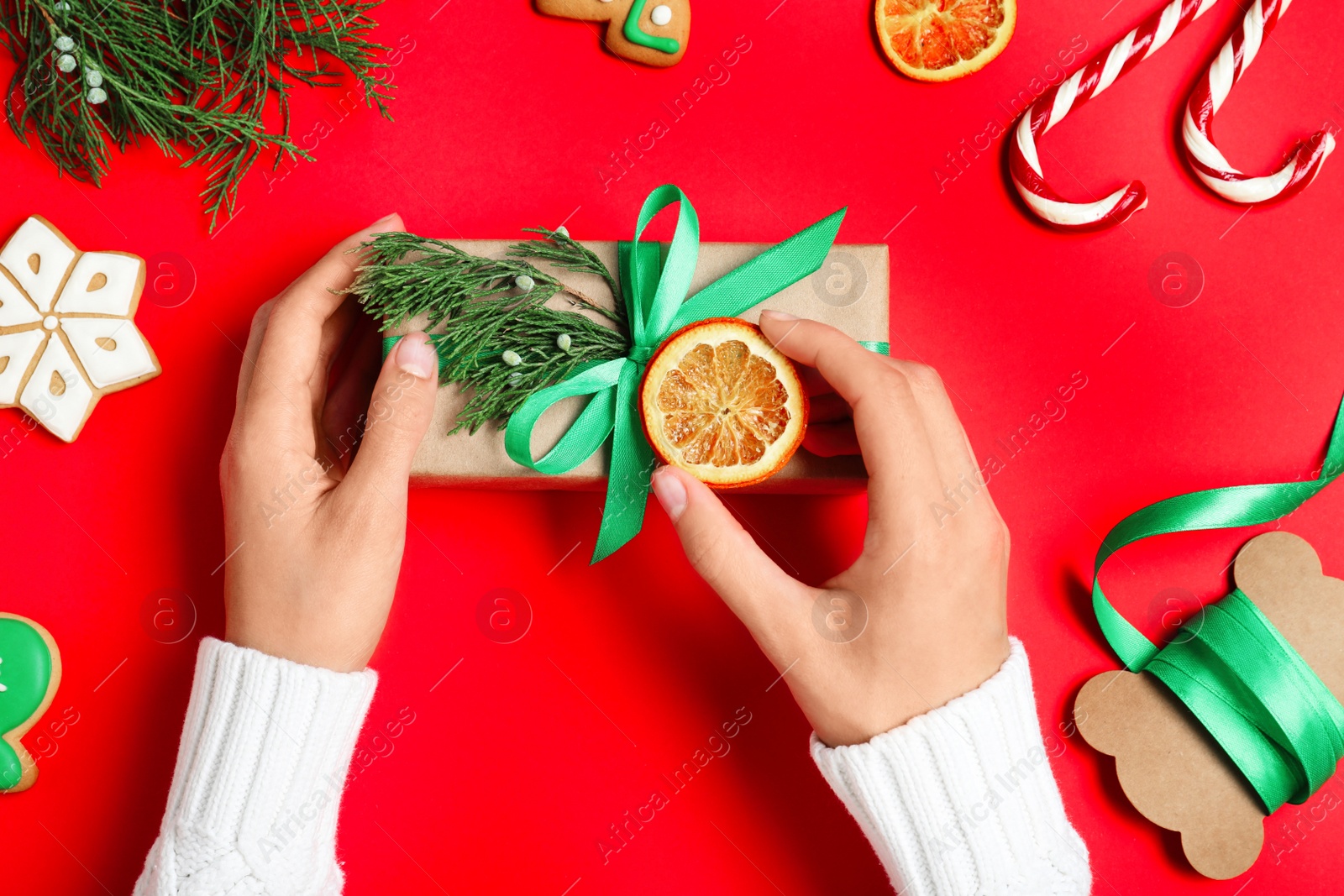 Photo of Woman wrapping Christmas gift on red background, top view