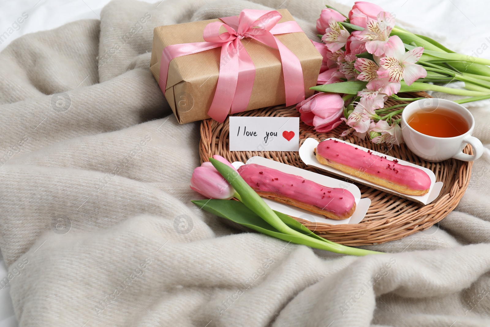 Photo of Tasty breakfast served in bed. Delicious eclairs, tea, flowers, gift box and card with phrase I Love You on blanket