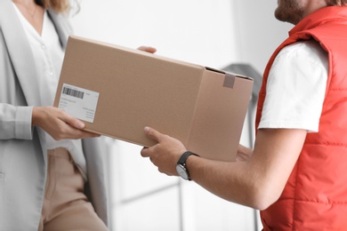 Photo of Young woman receiving parcel from courier indoors