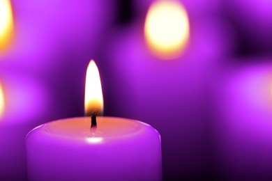 Burning violet candle on blurred background, closeup. Funeral attributes