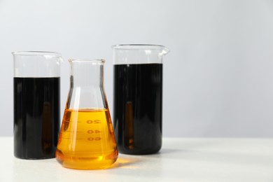 Beakers and flask with different types of oil on white table, space for text