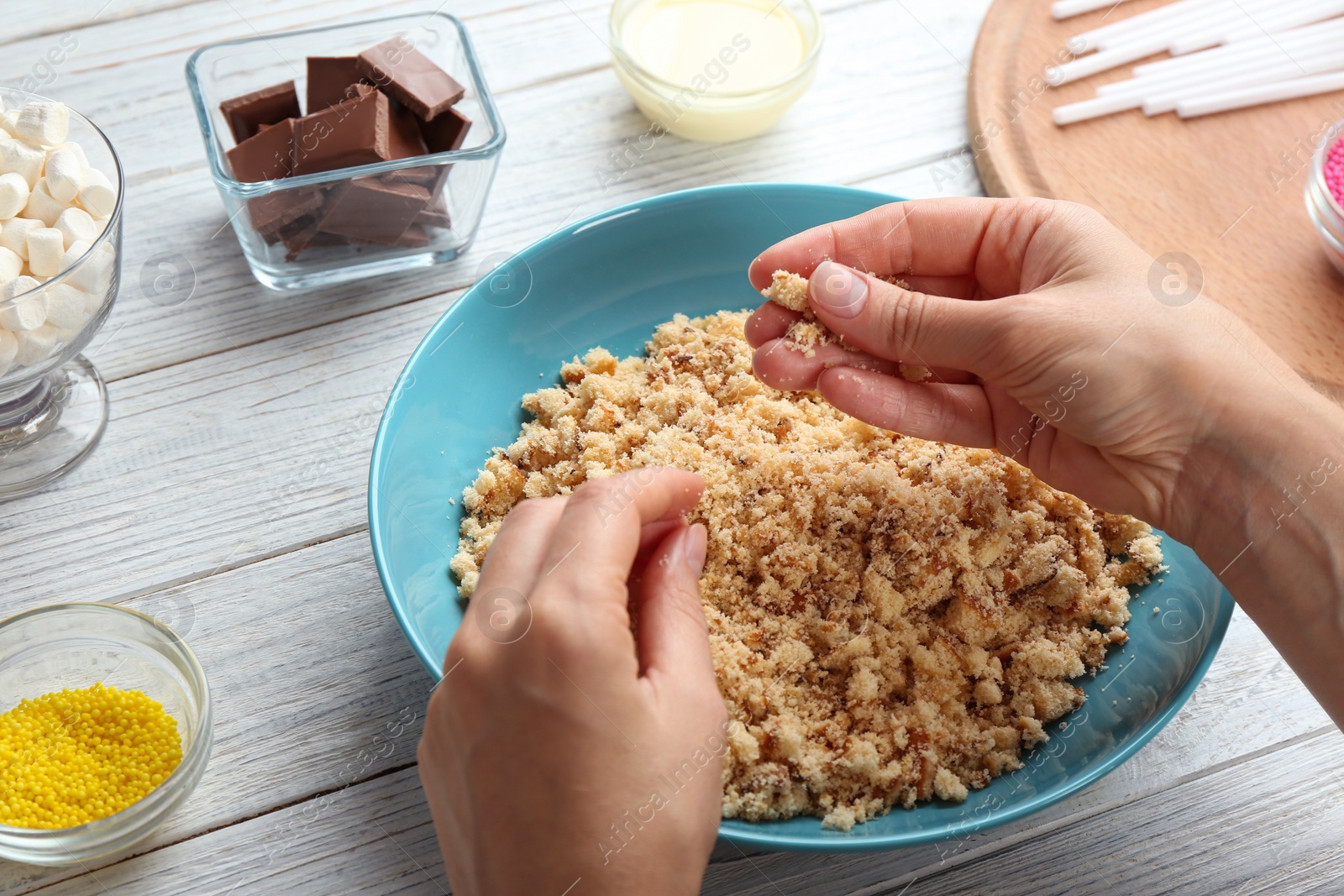 Photo of Woman making tasty cake pops at white wooden table, closeup