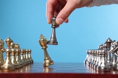 Photo of Man moving chess piece at checkerboard against light blue background, closeup