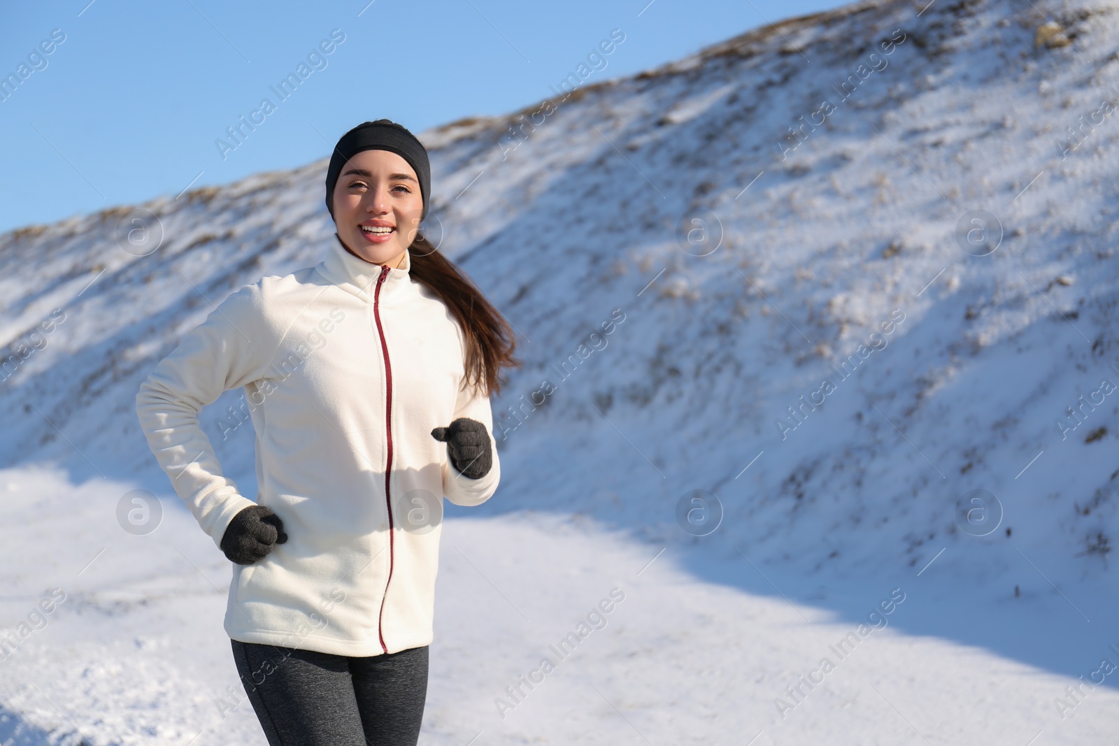 Photo of Happy woman running past snowy hill in winter. Outdoors sports exercises