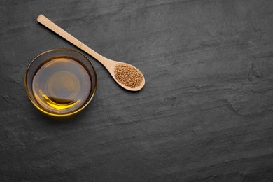 Photo of Bowl of natural oil and spoon with mustard seeds on black table, above view. Space for text