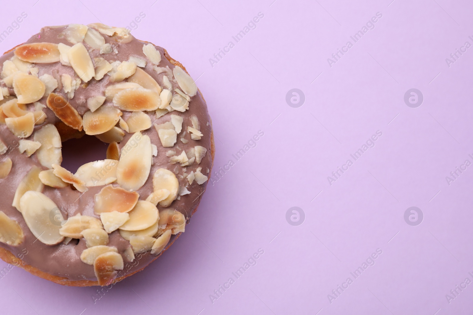 Photo of Tasty glazed donut decorated with nuts on purple background, top view. Space for text