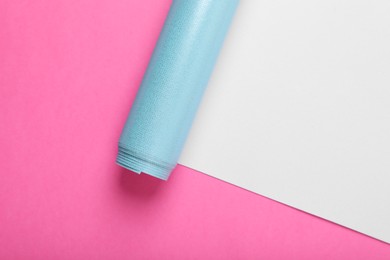 Roll of wrapping paper on pink background, top view