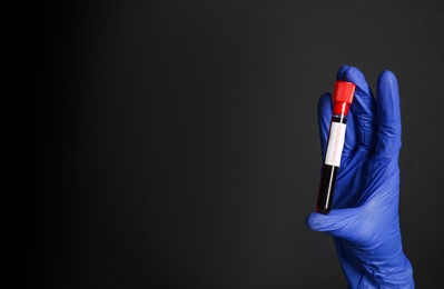 Photo of Scientist holding test tube with blood sample and label CORONA VIRUS on black background, closeup. Space for text