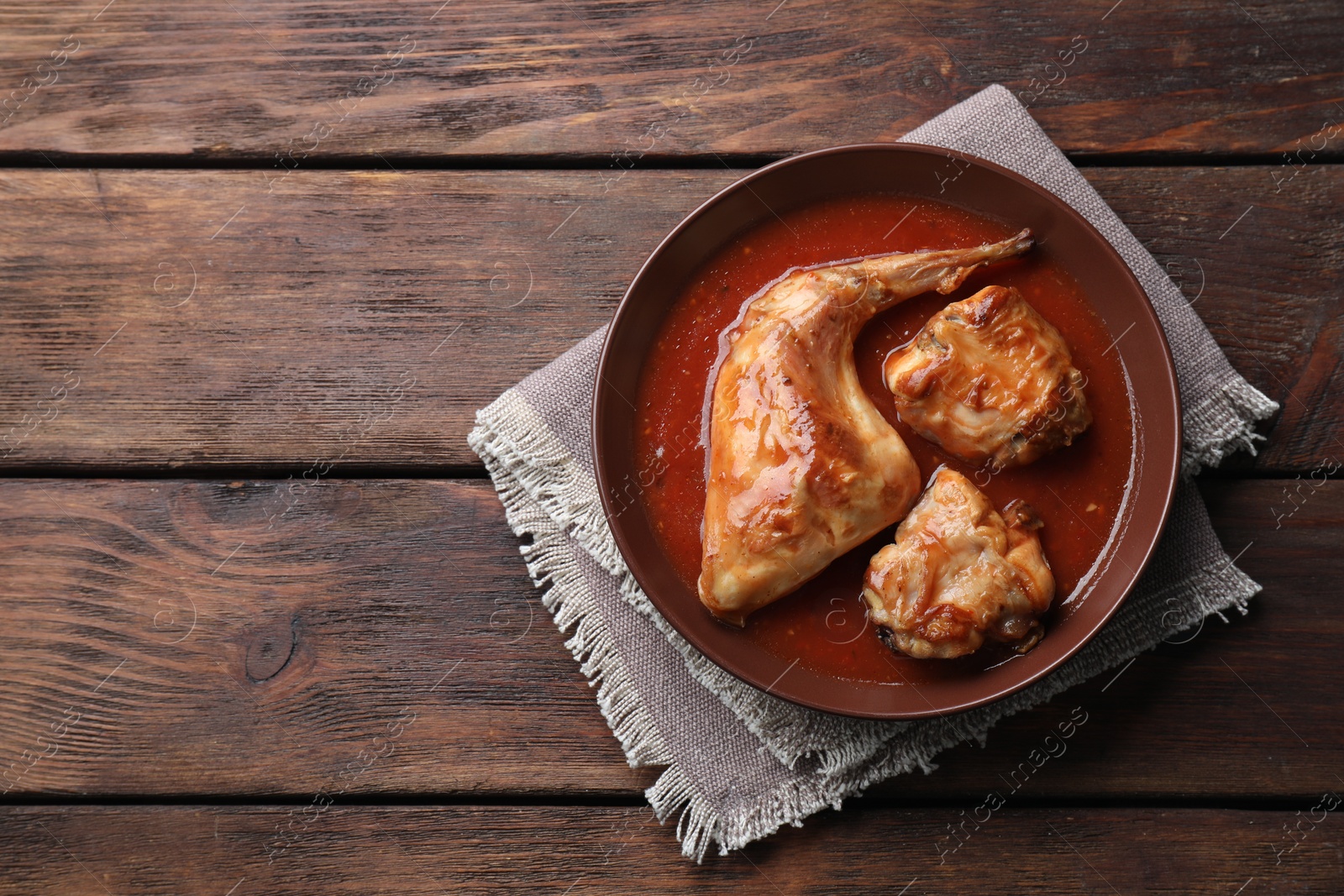 Photo of Tasty cooked rabbit meat with sauce on wooden table, top view. Space for text