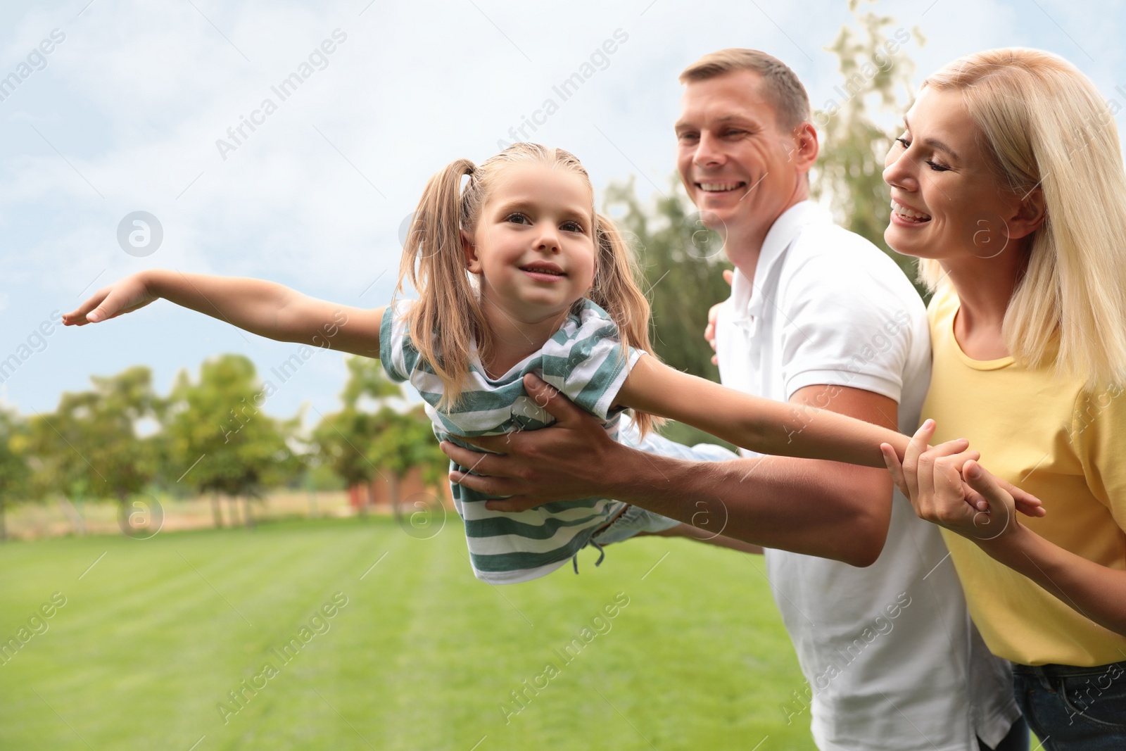 Photo of Cute little girl having fun with her parents in park on summer day