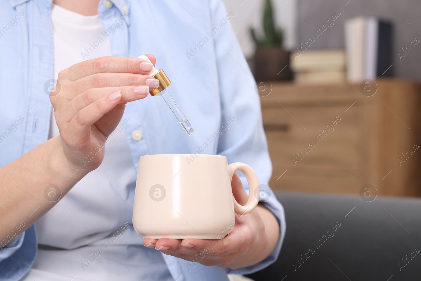 Photo of Woman dripping food supplement into cup indoors, closeup. Space for text