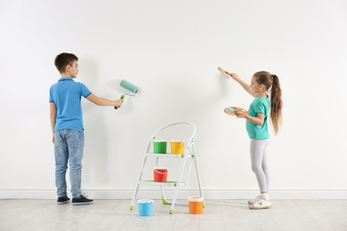 Photo of Little children painting on blank white wall indoors
