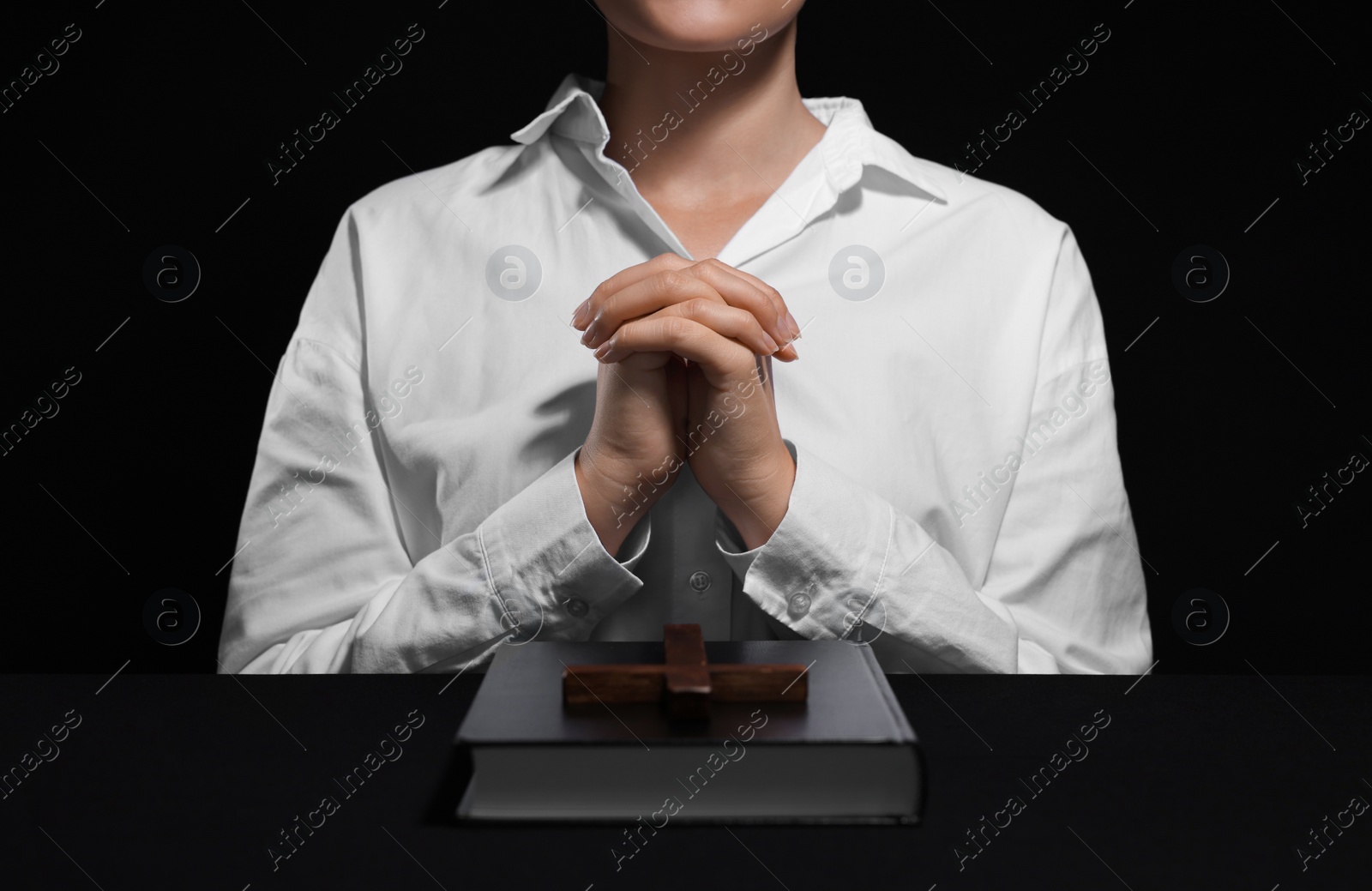 Photo of Woman holding hands clasped while praying at table with Bible and cross, closeup