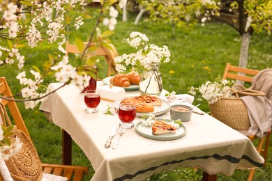 Stylish table setting with beautiful spring flowers, fruit drink and pie in garden