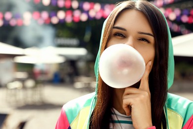 Photo of Beautiful young woman blowing chewing gum on city street outdoors