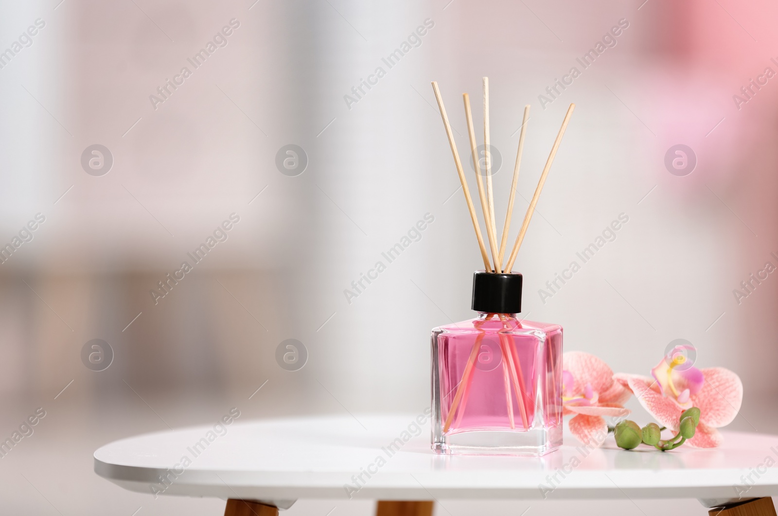 Photo of Aromatic reed air freshener and flowers on table against blurred background