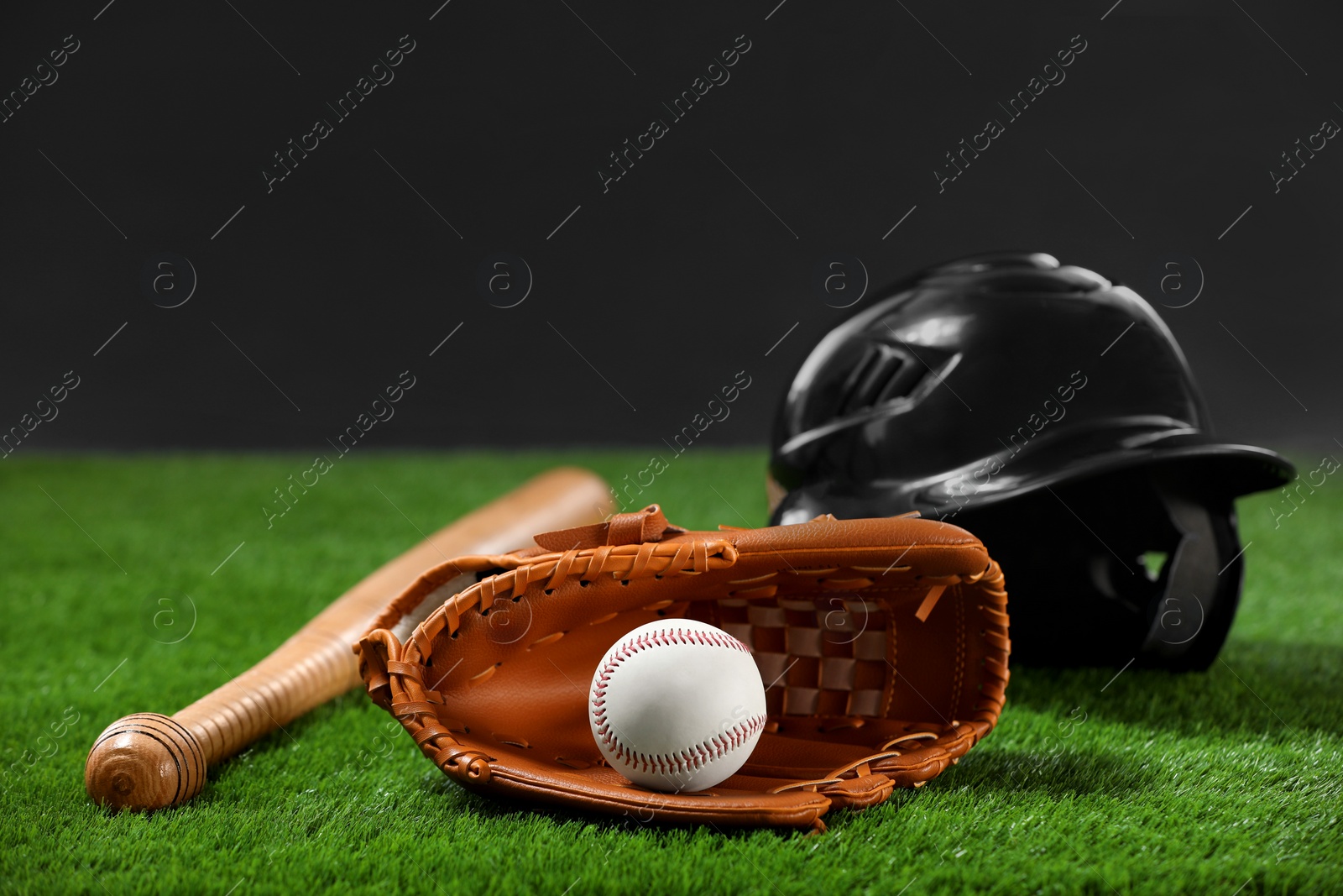 Photo of Baseball bat, batting helmet, leather glove and ball on green grass against dark background. Space for text