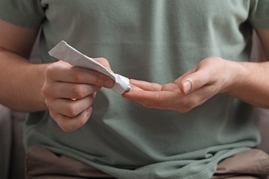 Man applying ointment from tube onto his fingers, closeup