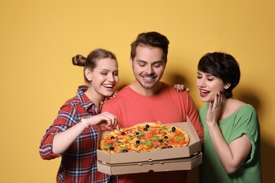 Group of friends with delicious pizza on color background