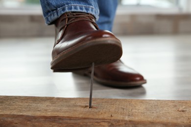 Careless man stepping on nail in wooden plank indoors, closeup