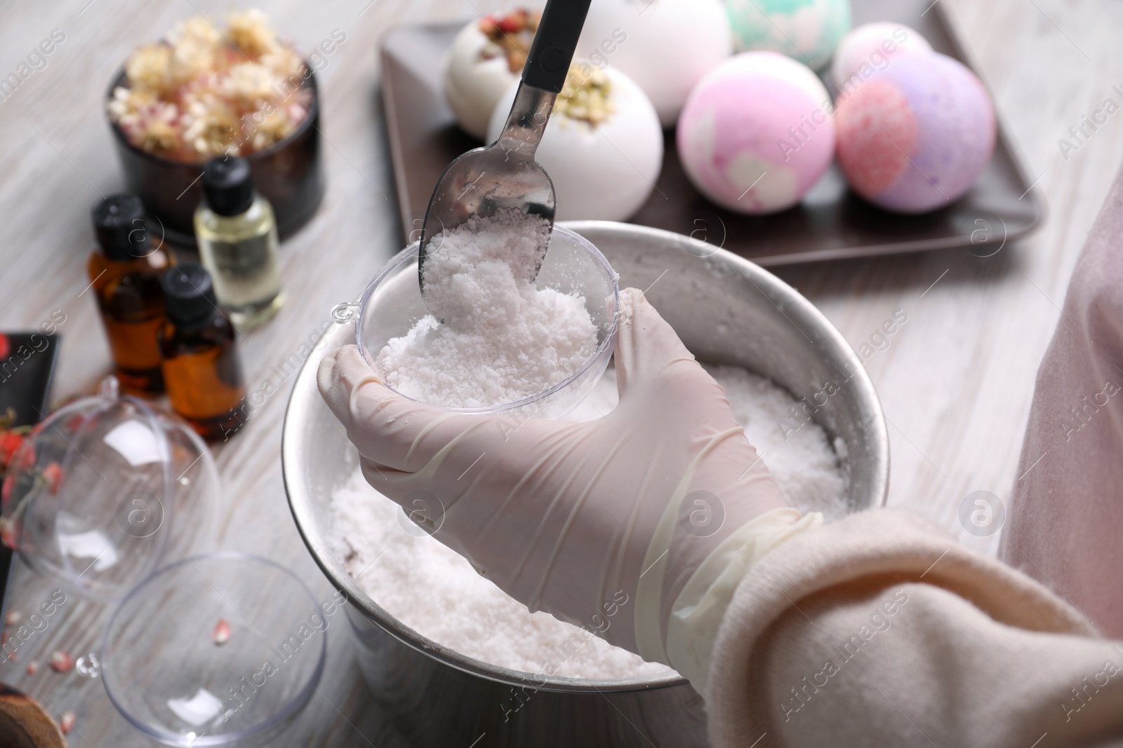 Photo of Woman in gloves making bath bomb at wooden table, closeup