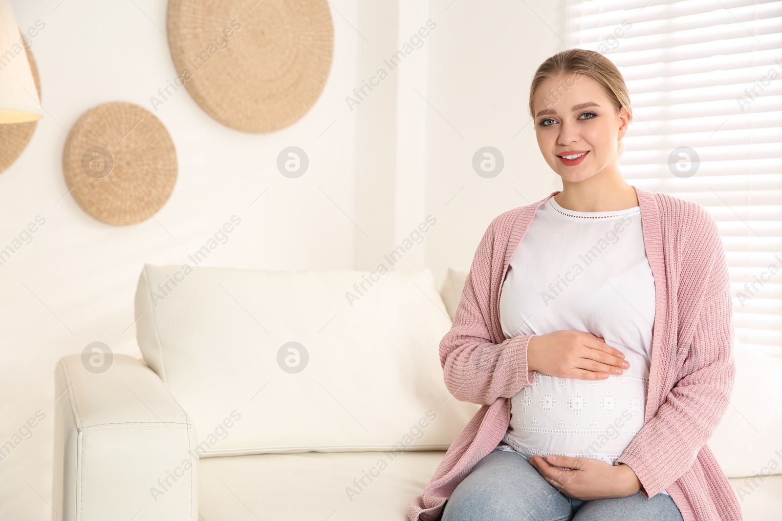 Photo of Young pregnant woman on sofa at home. Space for text