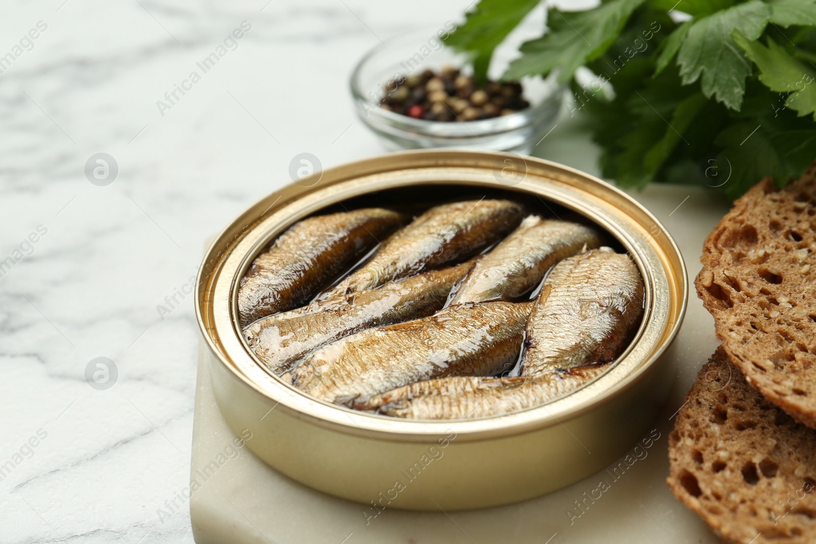 Photo of Tin can with tasty sprats served on white marble table, closeup. Space for text
