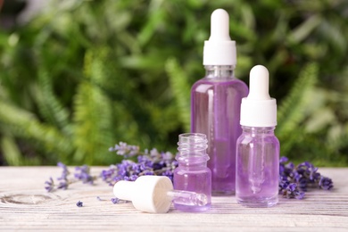 Bottles with natural lavender essential oil on white wooden table against blurred background. Space for text